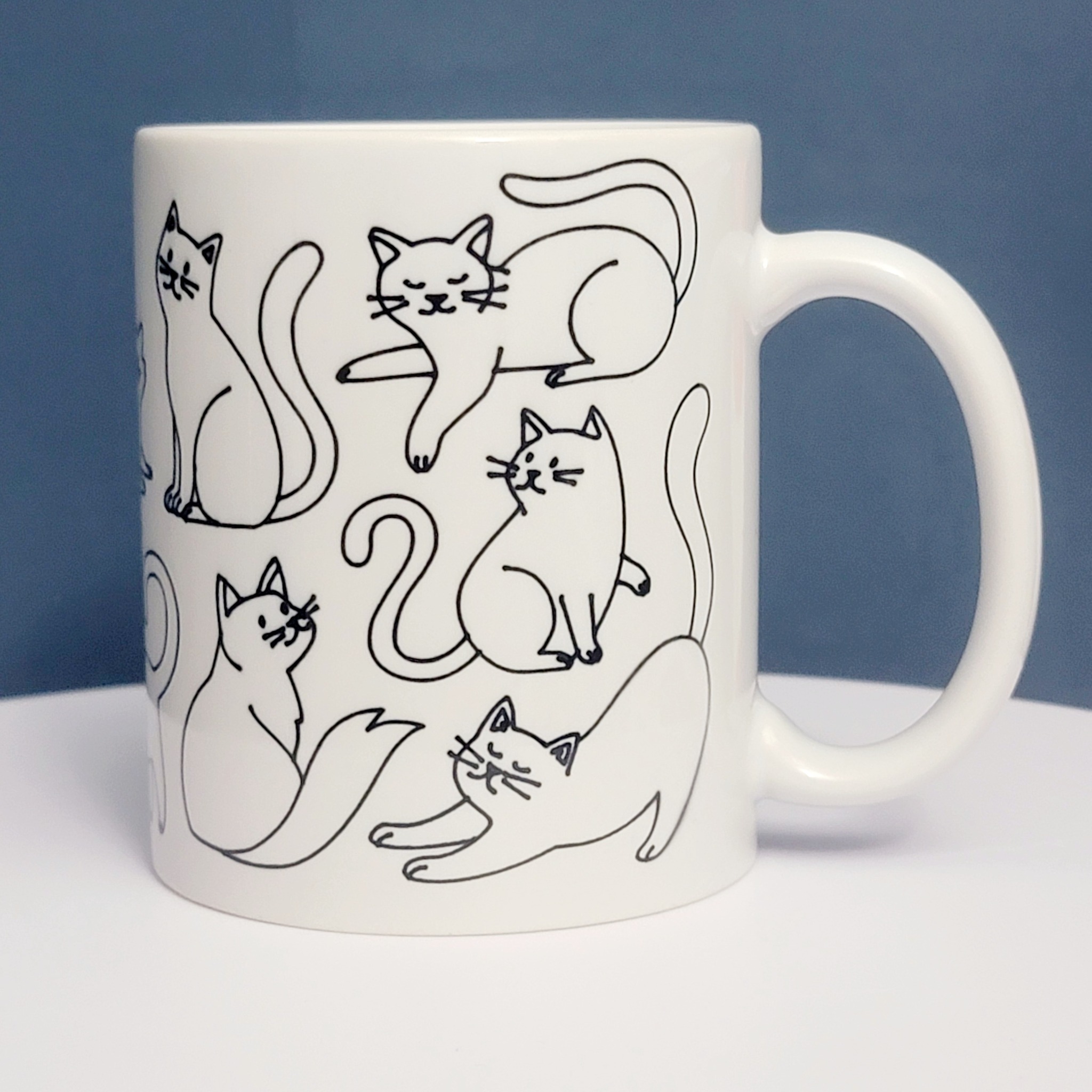 White ceramic mug with twelve playful black cat drawings